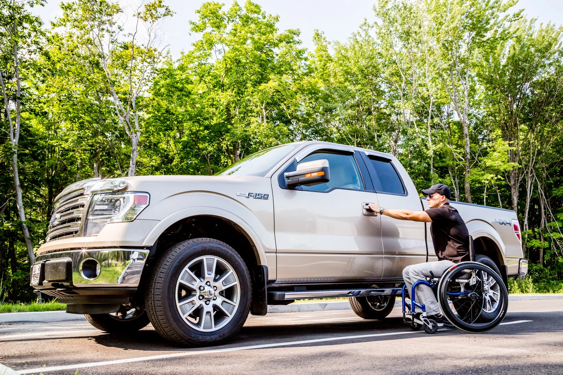 A man sitting in a rigid frame manual wheelchair is opening the door to a tan Ford pickup truck.